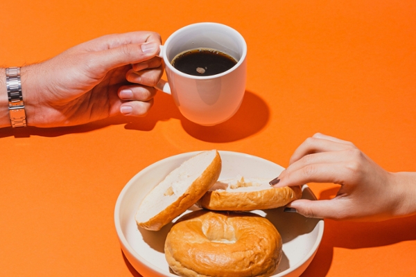 Two hands holding a coffee mug and a bagel.