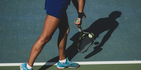 Shadow of a tennis player in shorts holding a racket. 