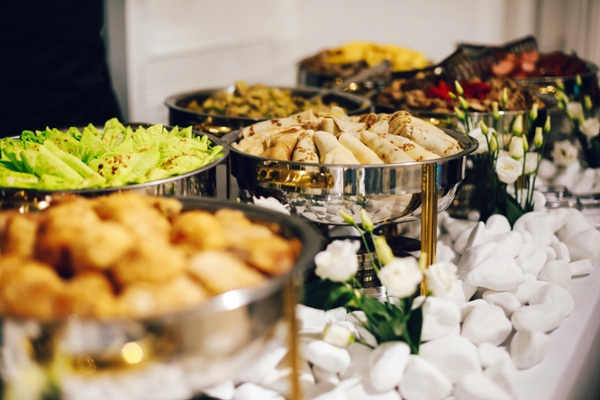 Catering table displaying trays of food and white flowers. 