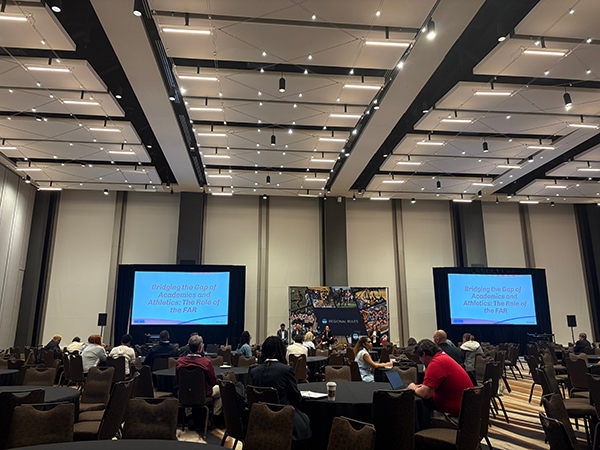 A wide view of a large conference hall in Atlanta with two large screens displaying the session title, "Bridging the Gap of Academics and Athletics: The Role of the FAR."