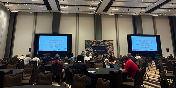 A wide view of a large conference hall in Atlanta with two large screens displaying the session title, "Bridging the Gap of Academics and Athletics: The Role of the FAR."