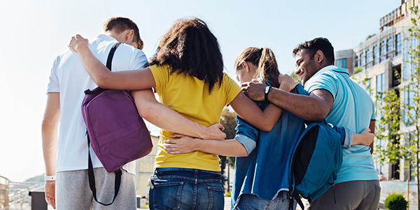 Image of four college students with their arms around each other and backs turned to the camera.