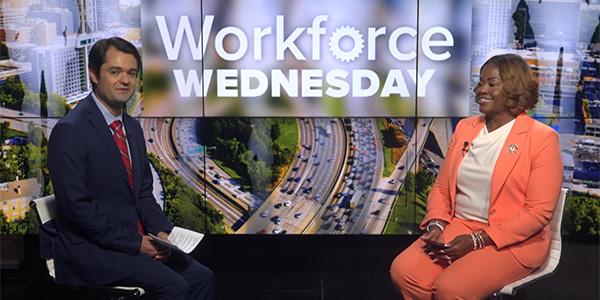 Image of Kristie Roberts-Lewis on a newscast set sitting in front of a screen alongside the news anchor that reads, "Workforce Wednesday."