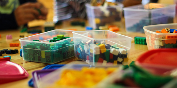 Clear plastic bins filled with colorful building bricks scattered across a wooden table.
