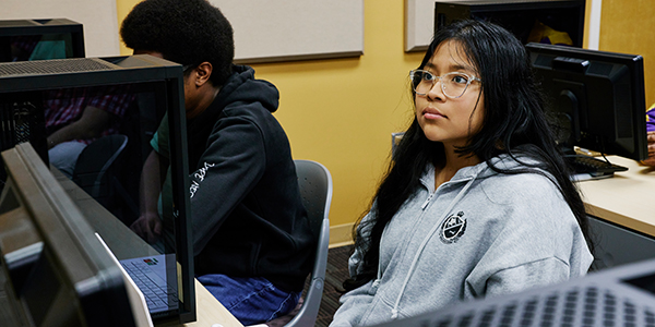Student sitting at a computer desk, attentively looking ahead.