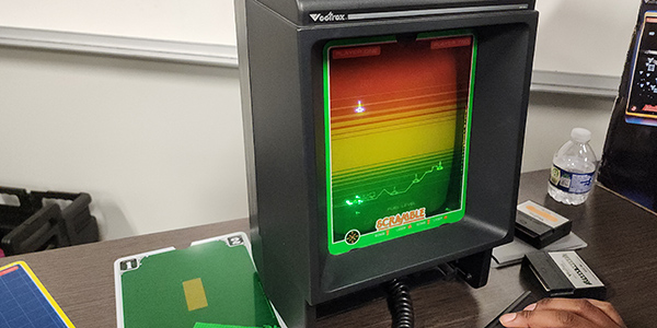 A Vectrex tabletop arcade console displaying a green and yellow retro game screen on a table. 