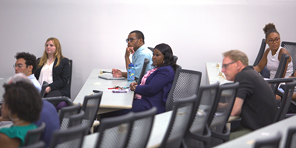Students sitting at desks in a classroom setting, listening to a presentation during the School of Business Innovation Pitch Competition.