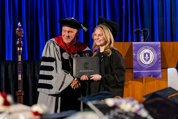 MGA Spring 2026 graduate posing with degree and President Blake.