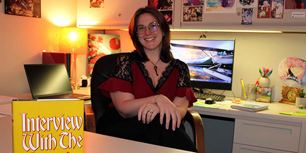 MGA professor, Dr. Storm Murray, poses for a photo at her desk with a cut-off yellow book stood up in front of her.